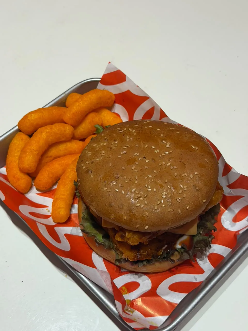 A double-stacked crispy chicken burger with cheese on a steel tray with cheese puffs