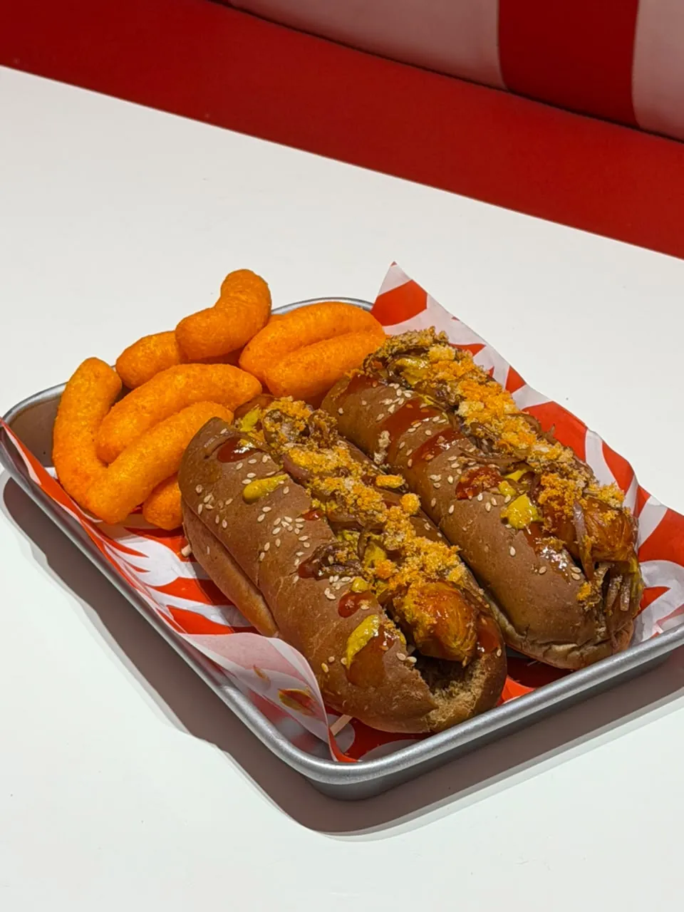 Two loaded chicken hot dogs with caramelised onions, mustard, ketchup and crumbs on sesame buns