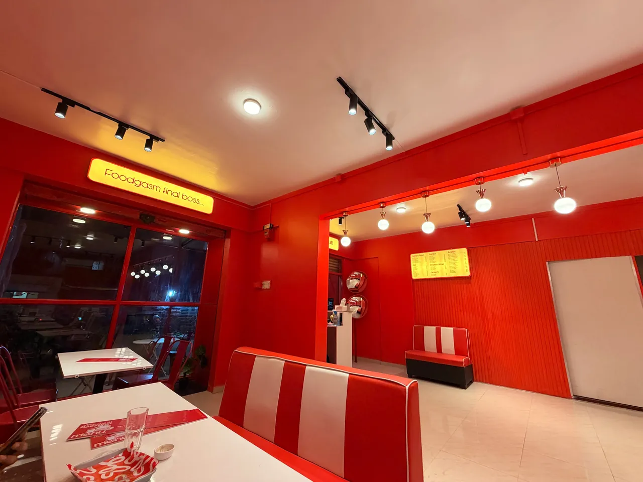 Inside Brioche & Beyond café in Kothrud with red walls, striped booth and a lit menu board